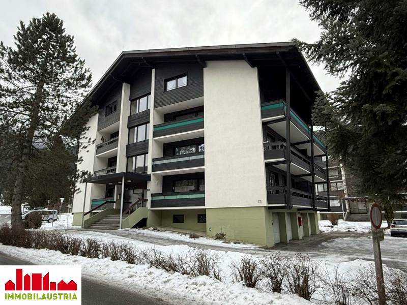 Gesamtansicht des modernen Apartmenthauses in einer verschneiten Berglandschaft.