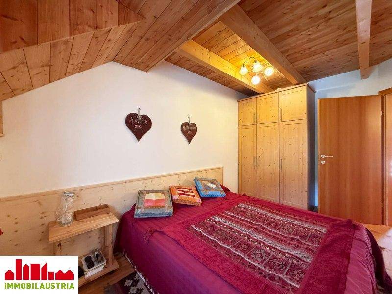 Schlafzimmer mit Holzbett, Einbauschränken und Holzbalkendecke unter der Dachschräge.