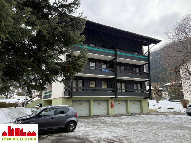 Ansicht des Apartmenthauses mit Balkonen und Garagen, umgeben von Bäumen und Schnee.
