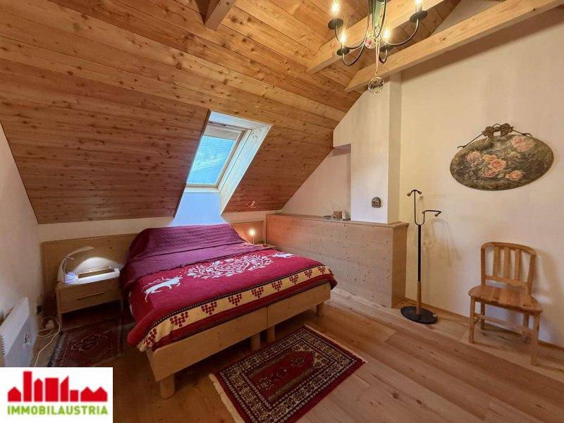 Schlafzimmer im Dachgeschoss mit Holzbalkendecke, Dachfenster und gemütlichem Bett.