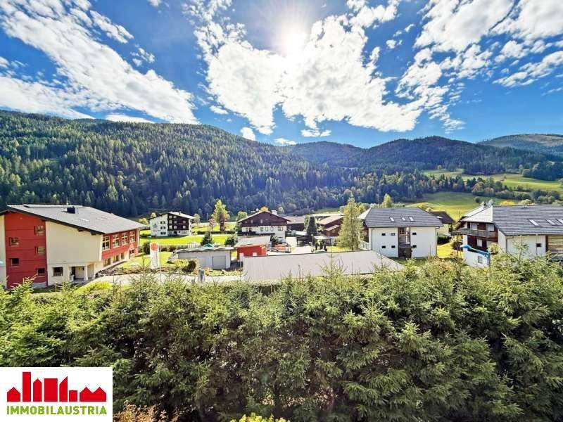 Panoramablick auf die grüne Berglandschaft und die umliegenden Häuser unter blauem Himmel.