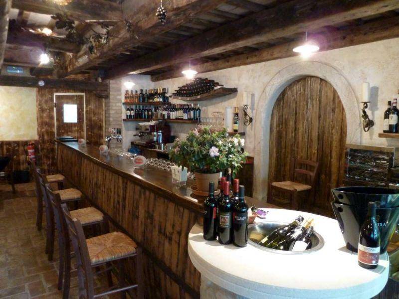 Lange Holztheke mit Barhockern und Weinflaschen, ergänzt durch eine rustikale Steinwand und Gewölbetür.