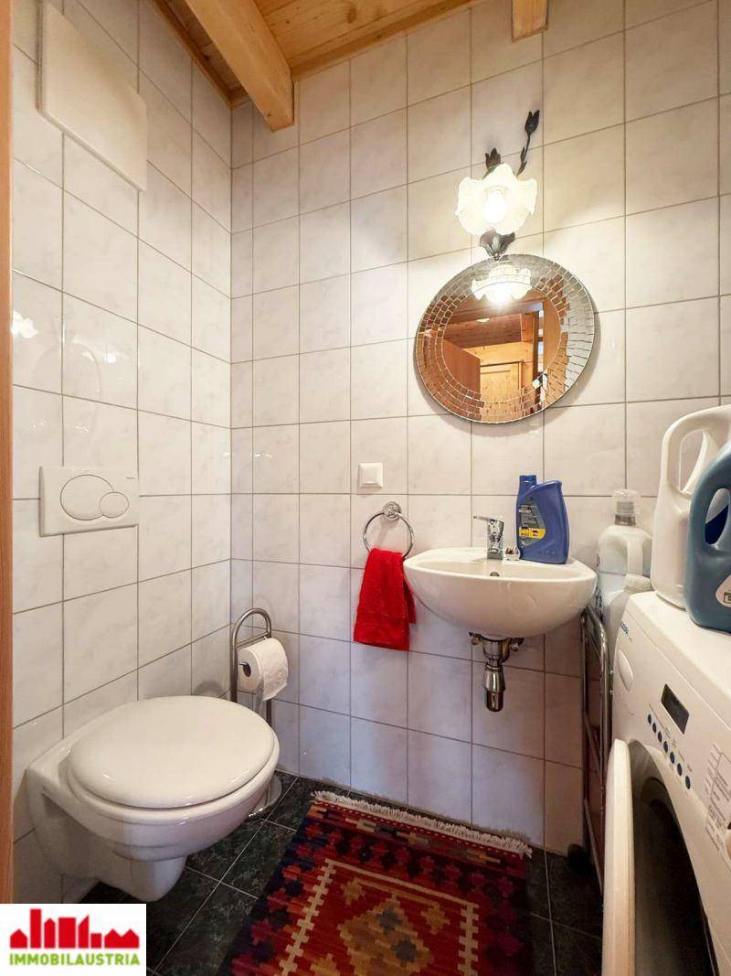 Kleines Badezimmer mit Toilette, Waschbecken und Waschmaschine, gefliest und funktional.