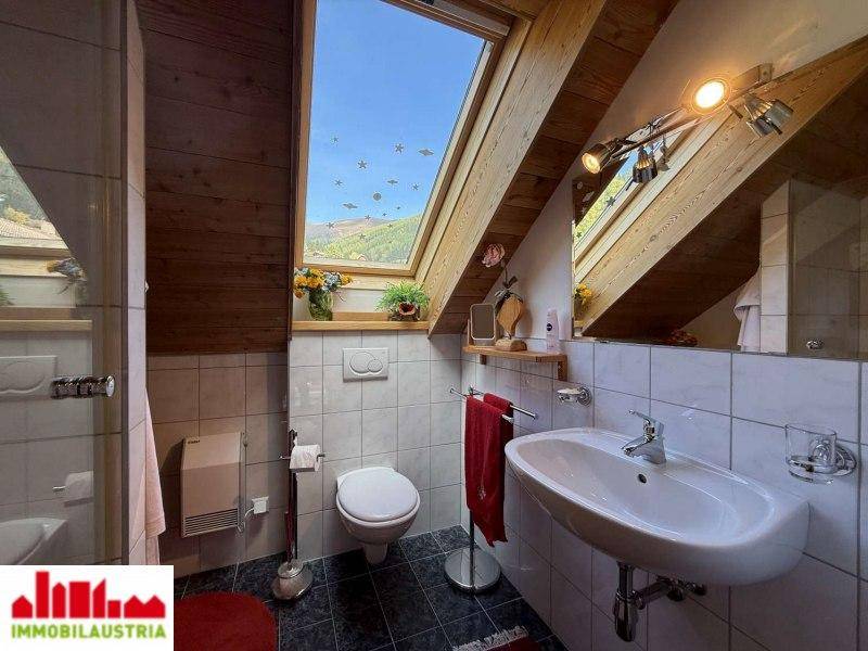 Badezimmer im Dachgeschoss mit Dachfenster, Waschbecken, Toilette und weißen Fliesen.