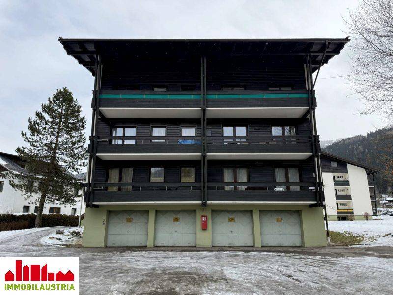 Mehrfamilienhaus mit mehreren Balkonen und Garagen im Erdgeschoss, umgeben von Schnee.