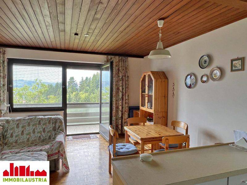 Wohn- und Essbereich mit Sofa, Holztisch und Zugang zu einem Balkon mit Aussicht.