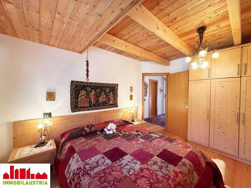 Schlafzimmer mit Holzbett, Einbauschränken und Holzbalkendecke unter der Dachschräge.
