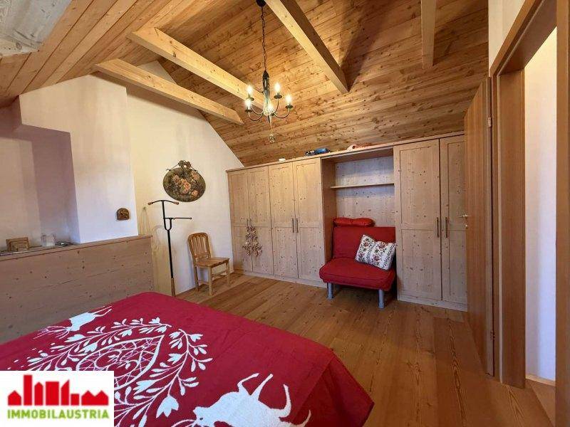 Geräumiges Schlafzimmer im Dachgeschoss mit Holzbalkendecke, Einbauschränken und Sitzgelegenheit.