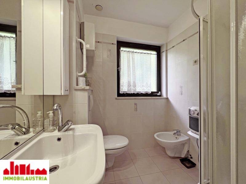 Badezimmer mit Fenster, Waschbecken, Toilette und Bidet, ausgestattet mit hellen Fliesen.