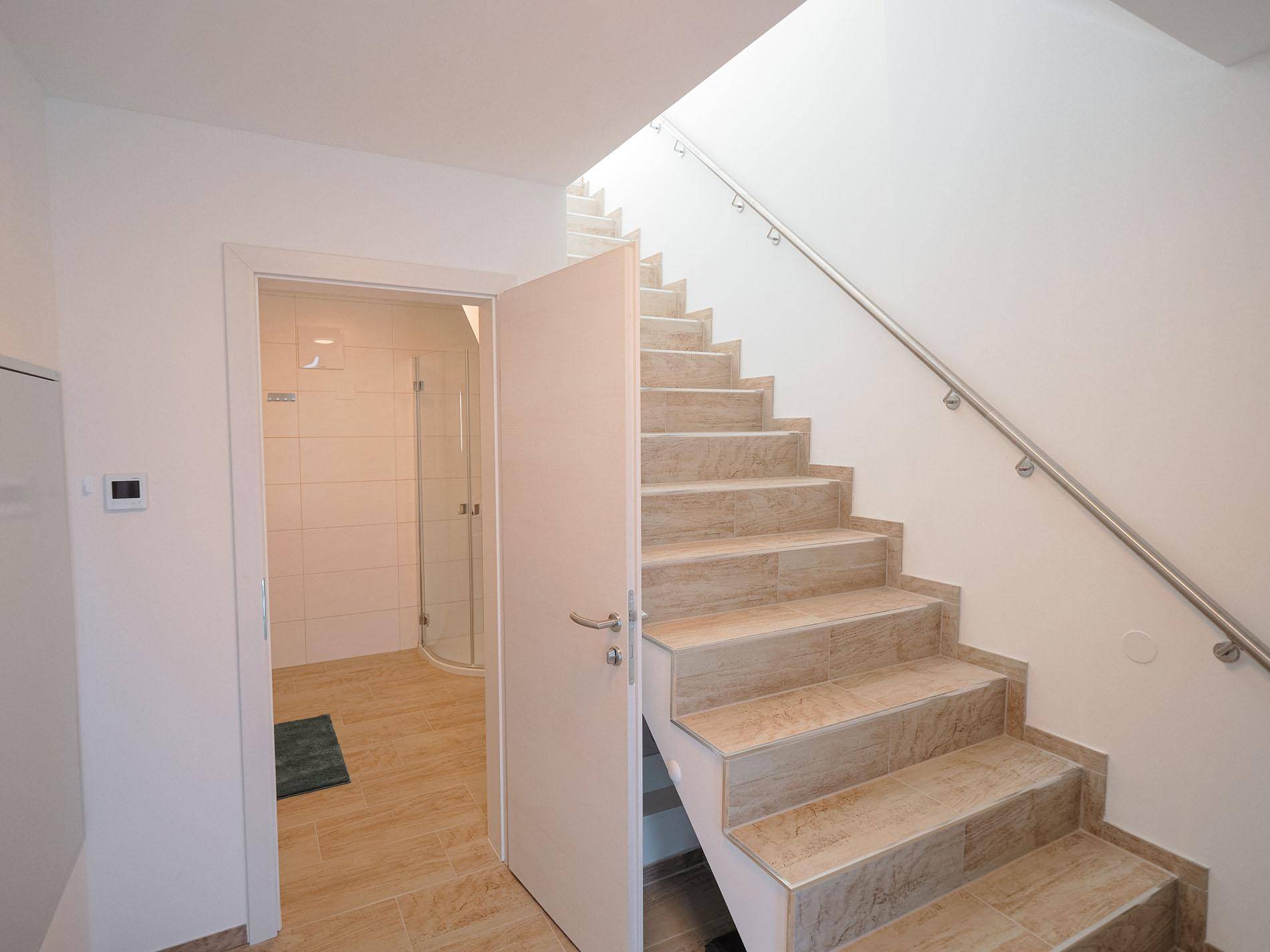 Heller Treppenaufgang mit Fliesenboden und Zugang zu einem modernen Badezimmer.