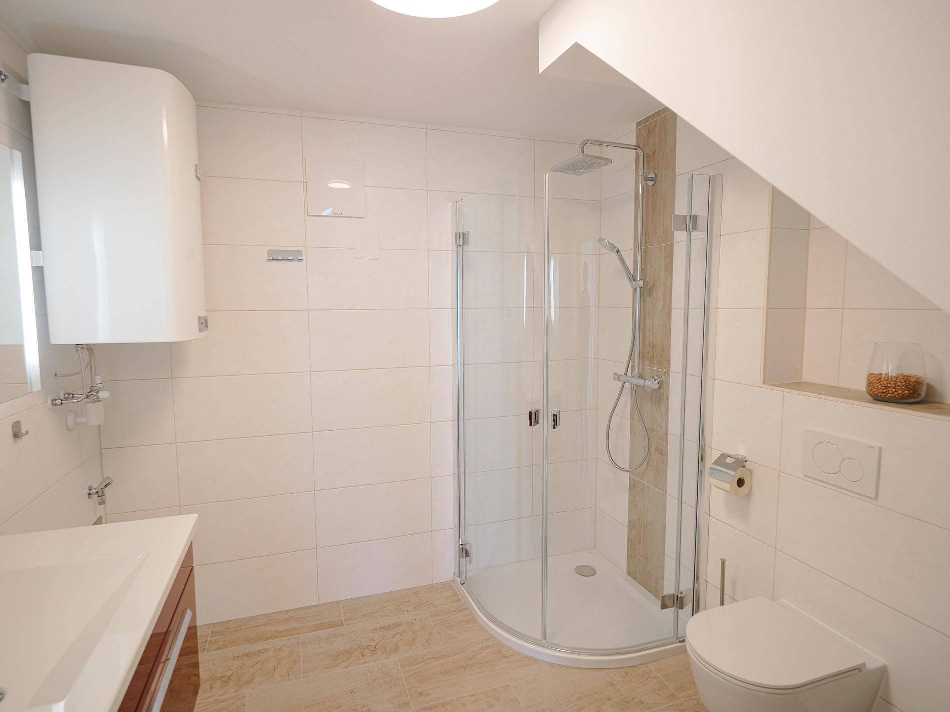 Modernes Badezimmer mit Duschkabine, Wand-WC und hellen Fliesen unter Dachschräge.