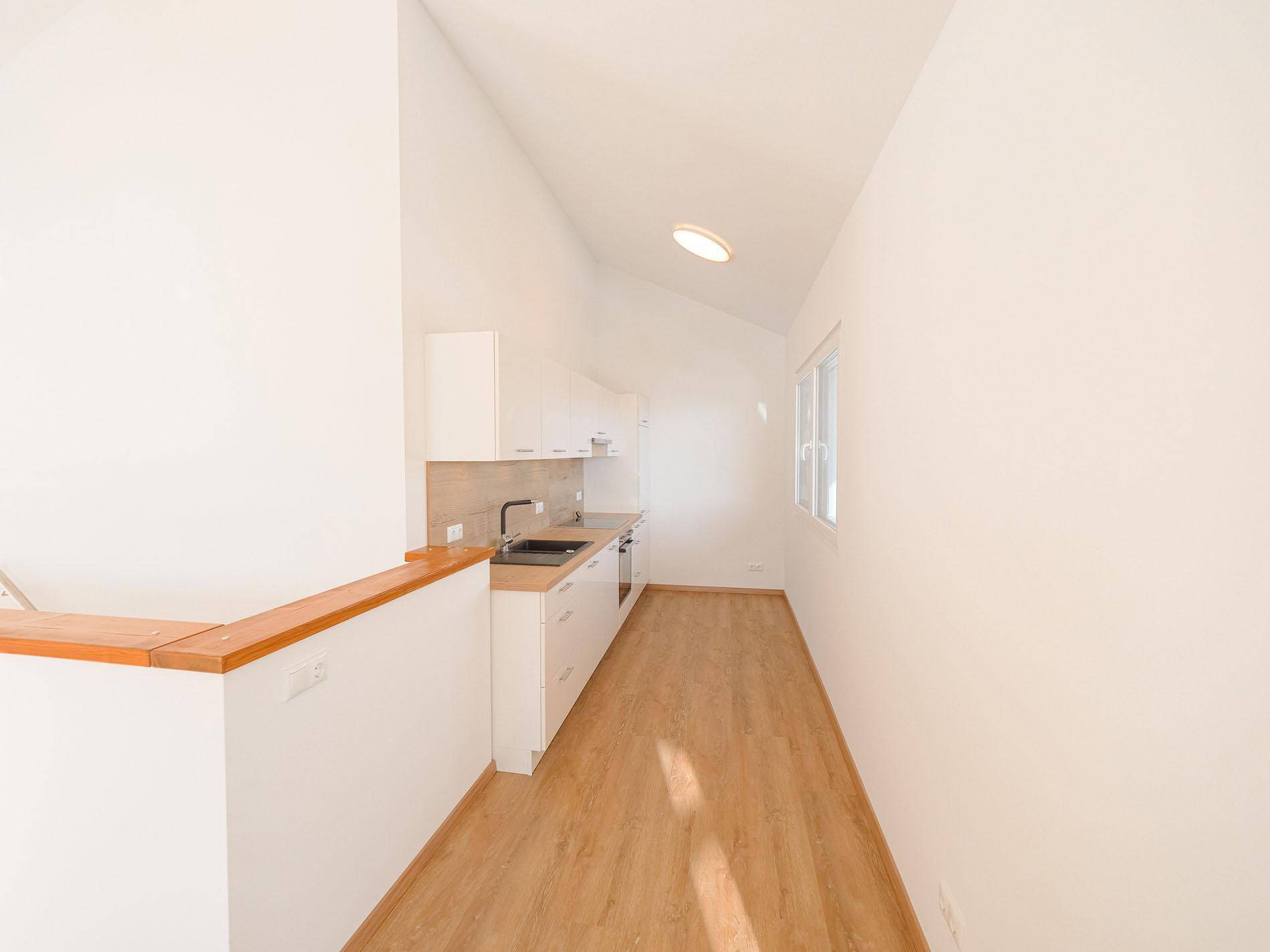 Schmale, helle Küche mit weißen Schränken und Holzarbeitsplatten in offenem Grundriss.