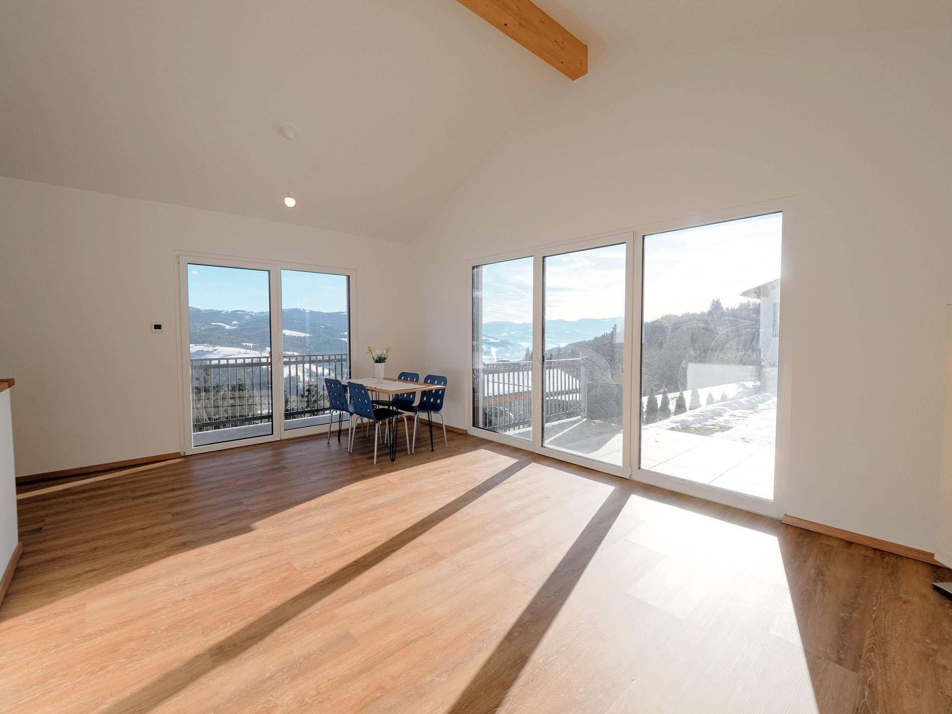 Lichtdurchfluteter Wohnbereich mit Panoramablick auf die verschneite Berglandschaft durch große Fenster.