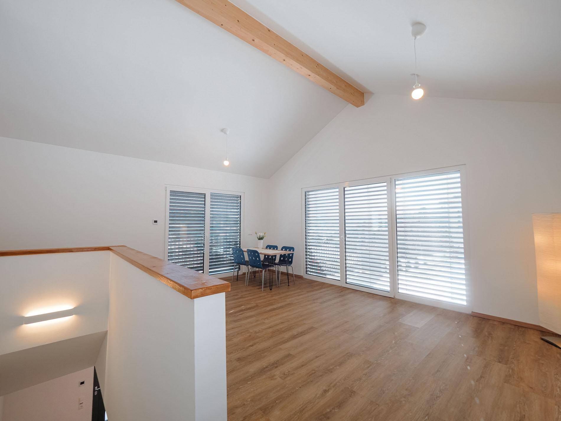 Geräumiger Wohn-Essbereich mit hohen Decken, Holzbalken und großen Fenstern.