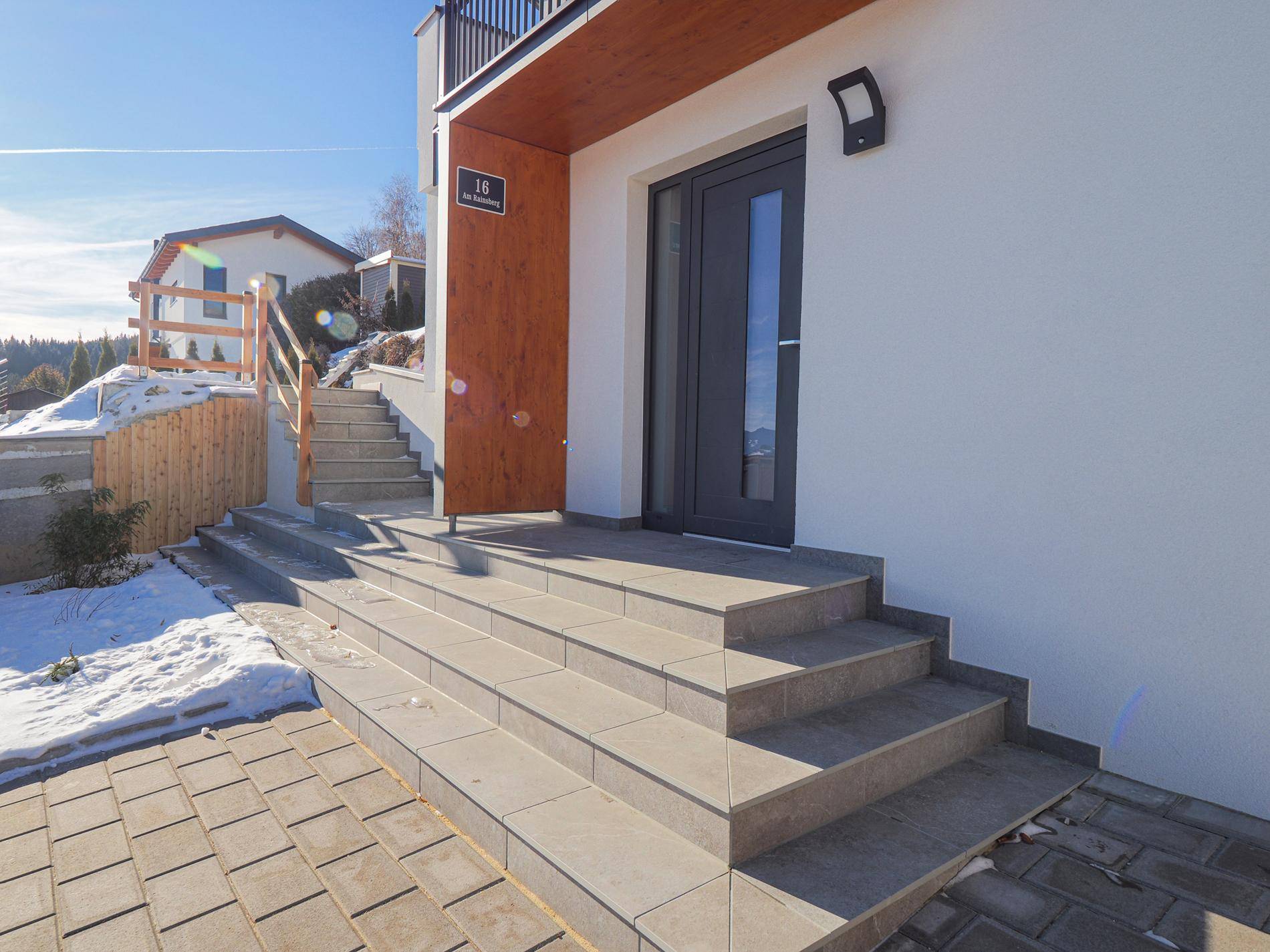 Eingangsbereich des Hauses mit Treppe, Holzelementen und gepflastertem Zugang.