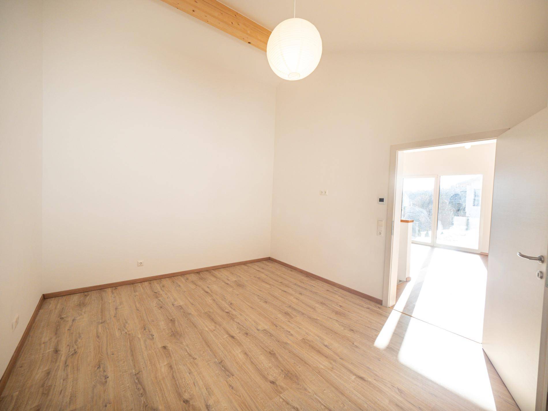 Leeres Zimmer mit Holzboden, hohen Decken und viel natürlichem Licht.