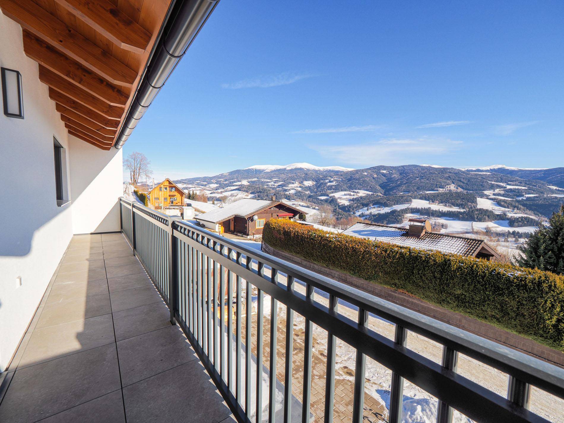 Geräumiger Balkon mit Panoramablick auf die winterliche Bergwelt und umliegende Häuser.