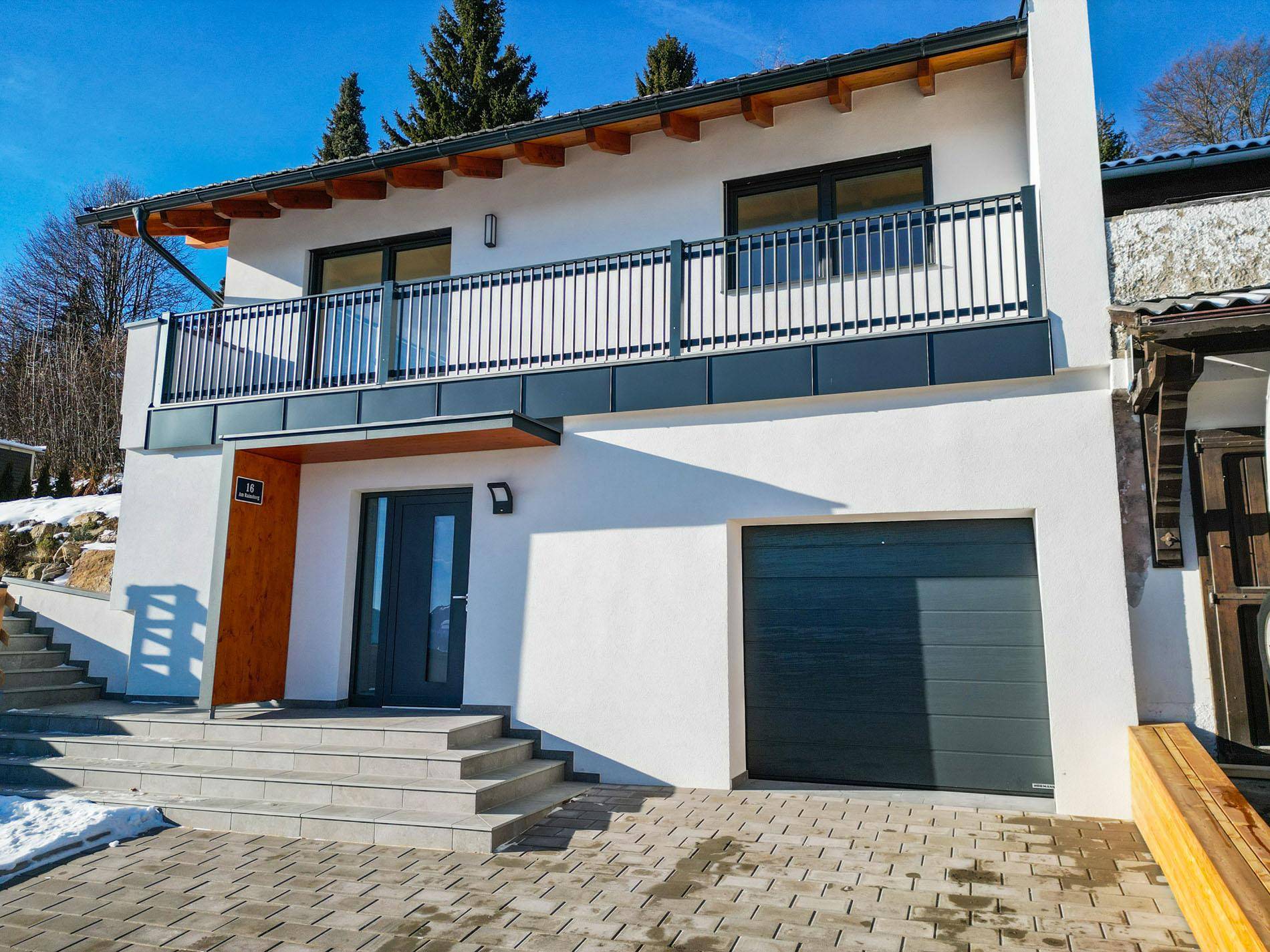 Moderne Hausfassade mit integrierter Garage, einladendem Eingangsbereich und großem Balkon.