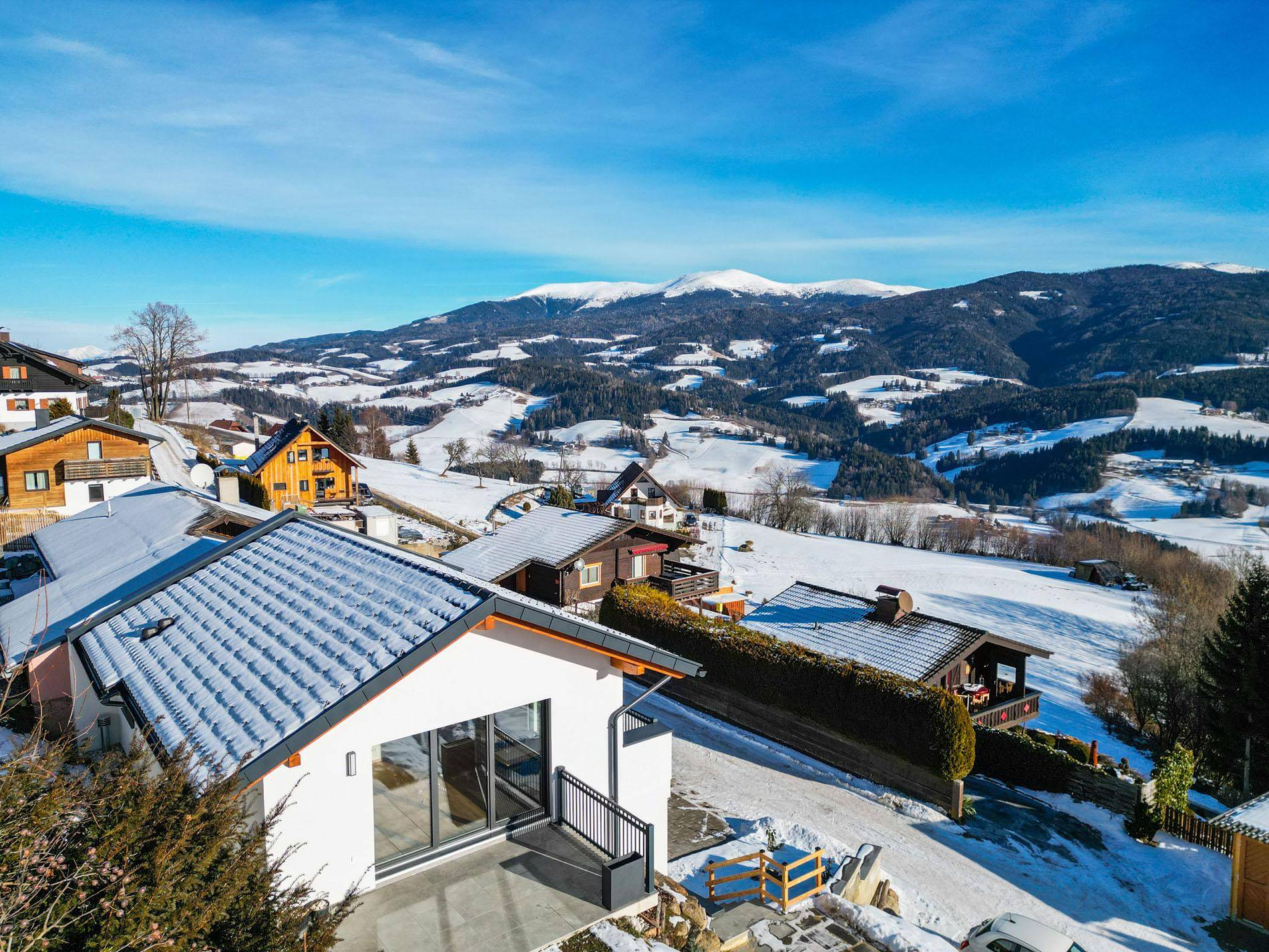 Weitläufige Luftaufnahme des Hauses in einer verschneiten Wohngegend mit Bergblick.