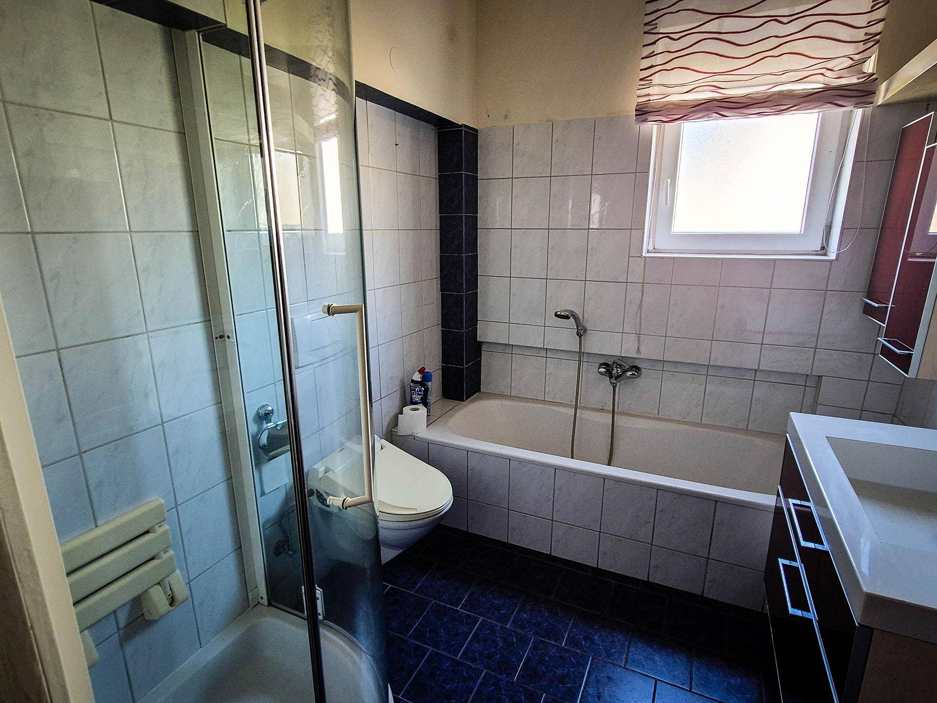 Badezimmer mit Badewanne, Dusche, WC und Fenster in einem älteren, aber gepflegten Stil.