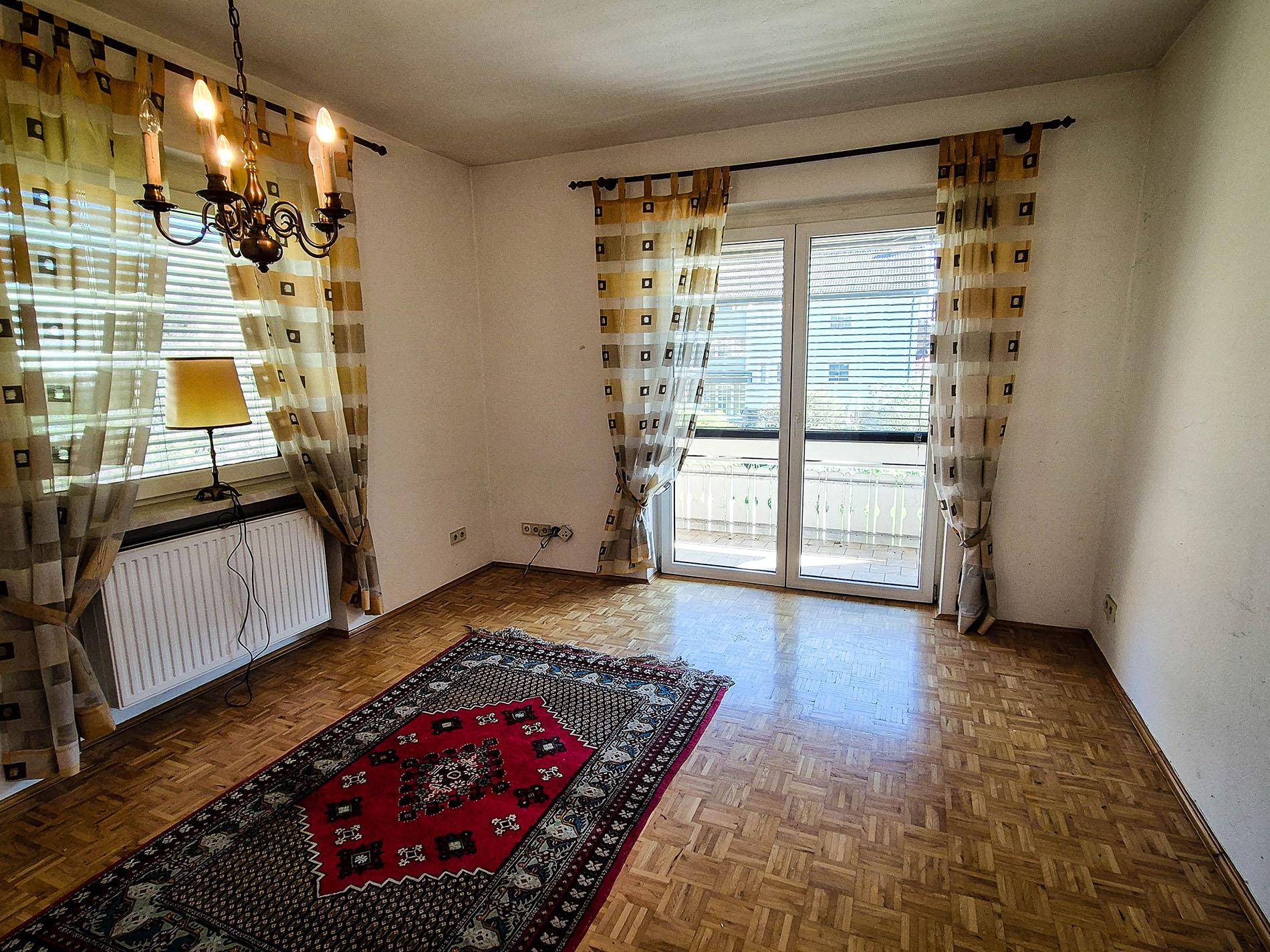 Helles Zimmer mit Parkettboden, großen Fenstern und Zugang zu einem französischen Balkon.