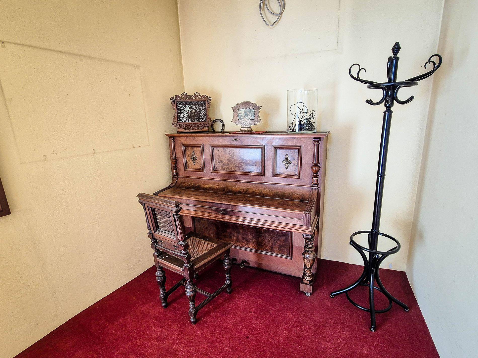 Flurbereich mit antikem Klavier, Garderobe und rotem Teppichboden.