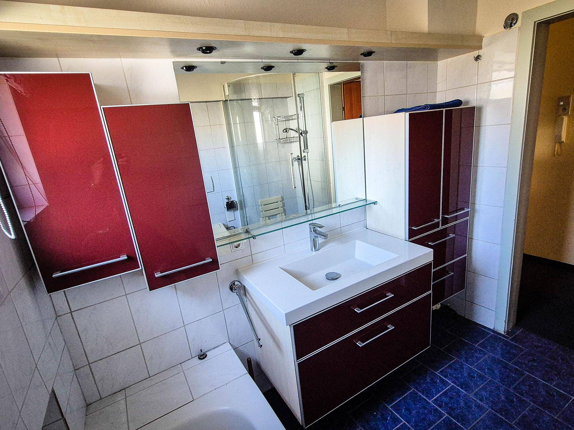 Badezimmer mit modernem Waschtisch, Spiegelschrank und roten Hochschränken.