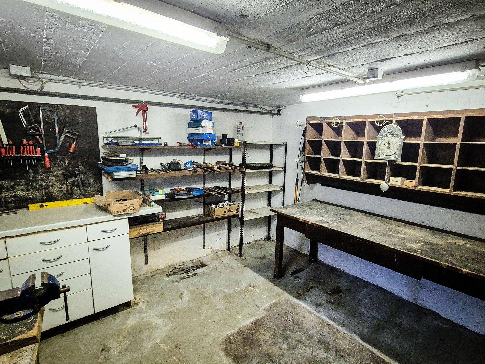 Geräumige Werkstatt im Keller mit Regalen, Werkbank und verschiedenen Werkzeugen.