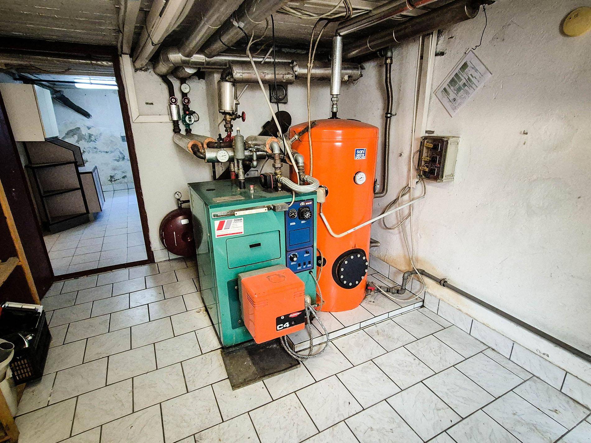 Heizungsraum im Keller mit Heizkessel, Warmwasserspeicher und Fliesenboden.
