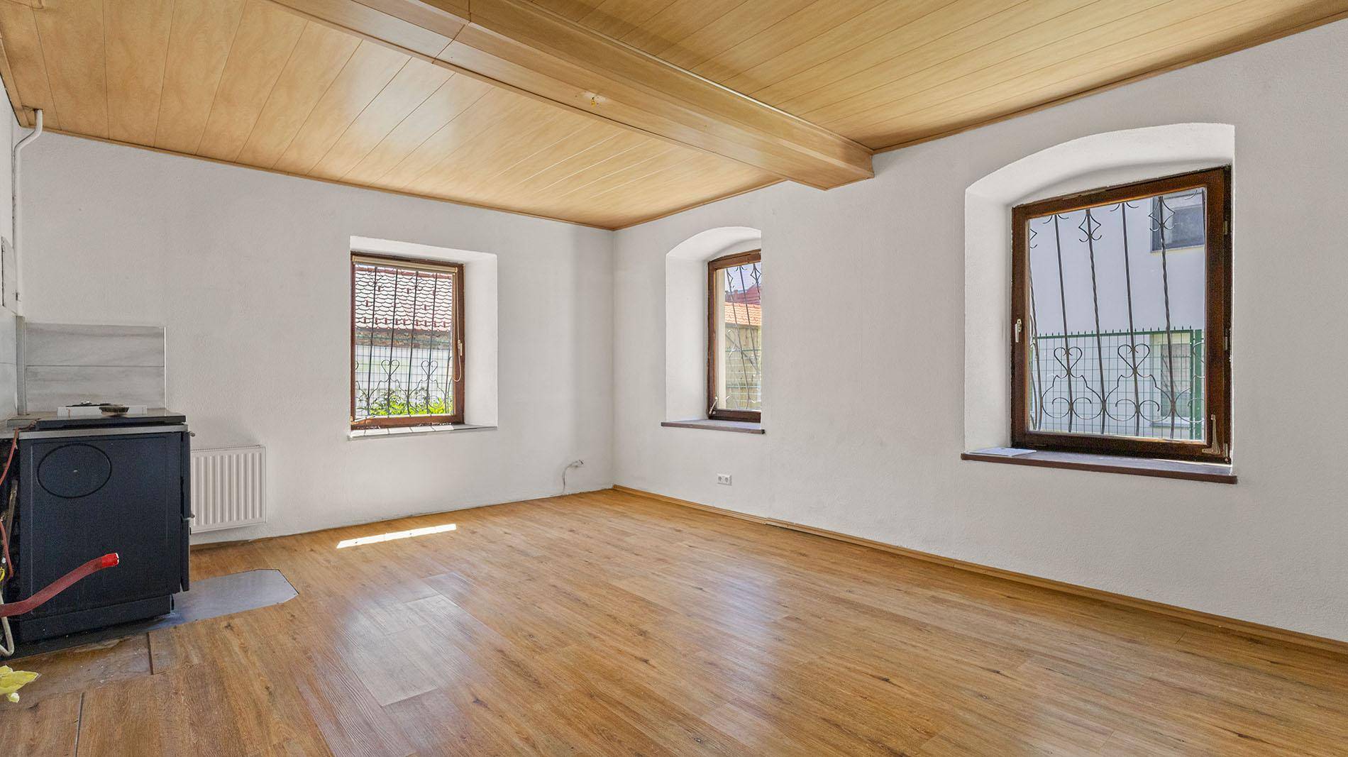 Helles Wohnzimmer mit Holzbalkendecke, Holzofen und Parkettboden.