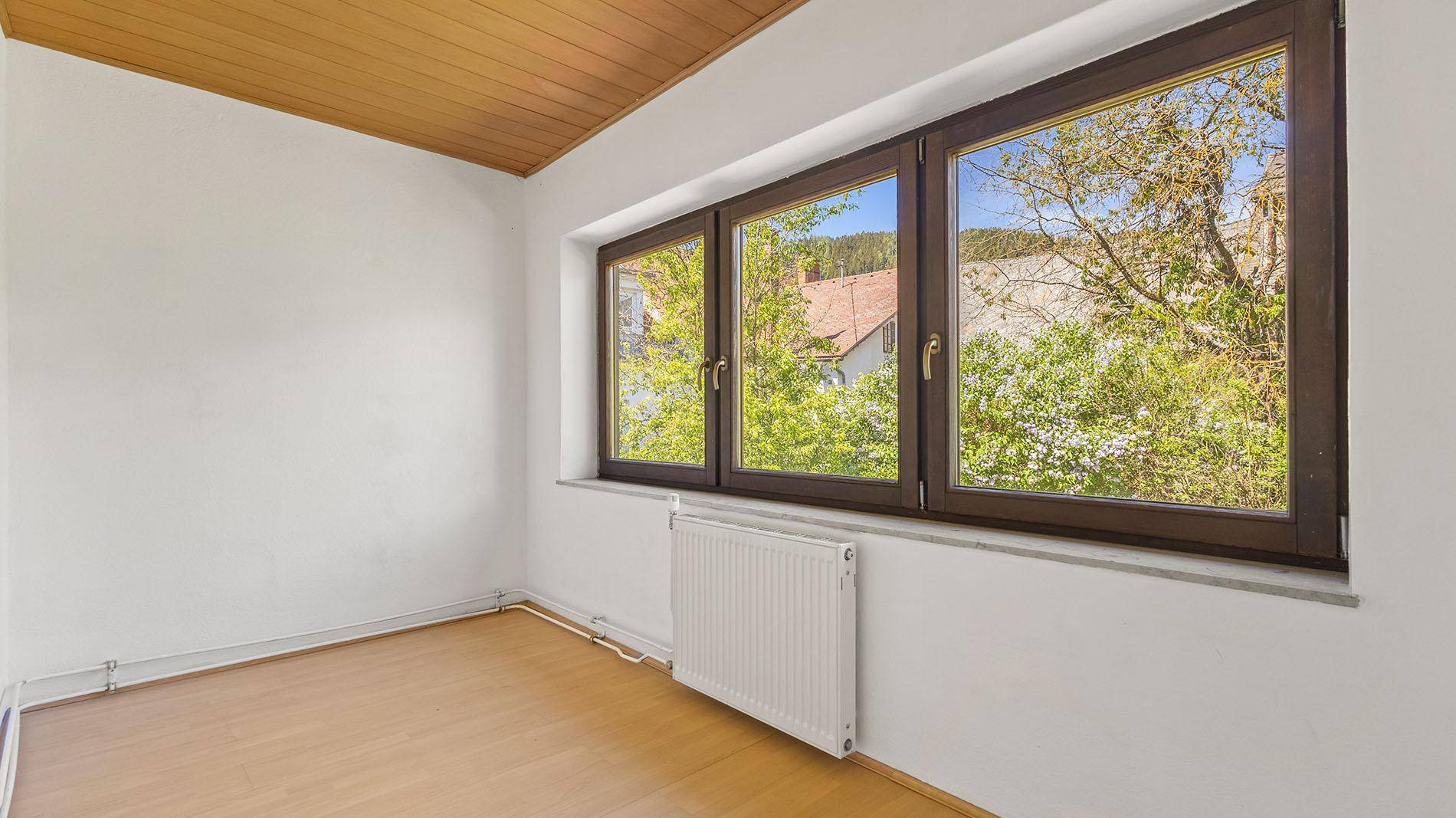 Schlafzimmer mit breitem Fenster, Holzboden und Blick ins Grüne.