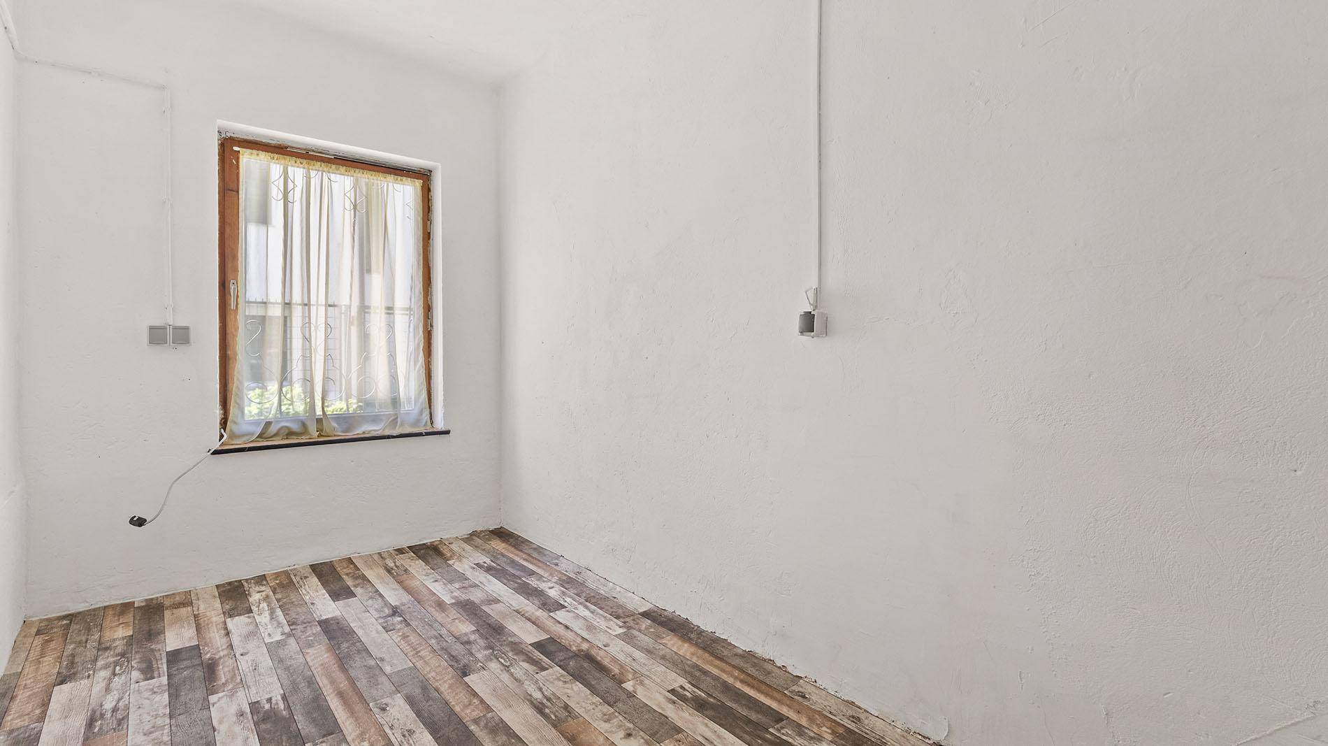 Kleines Zimmer mit rustikalem Holzboden und einem Fenster mit Vorhang.