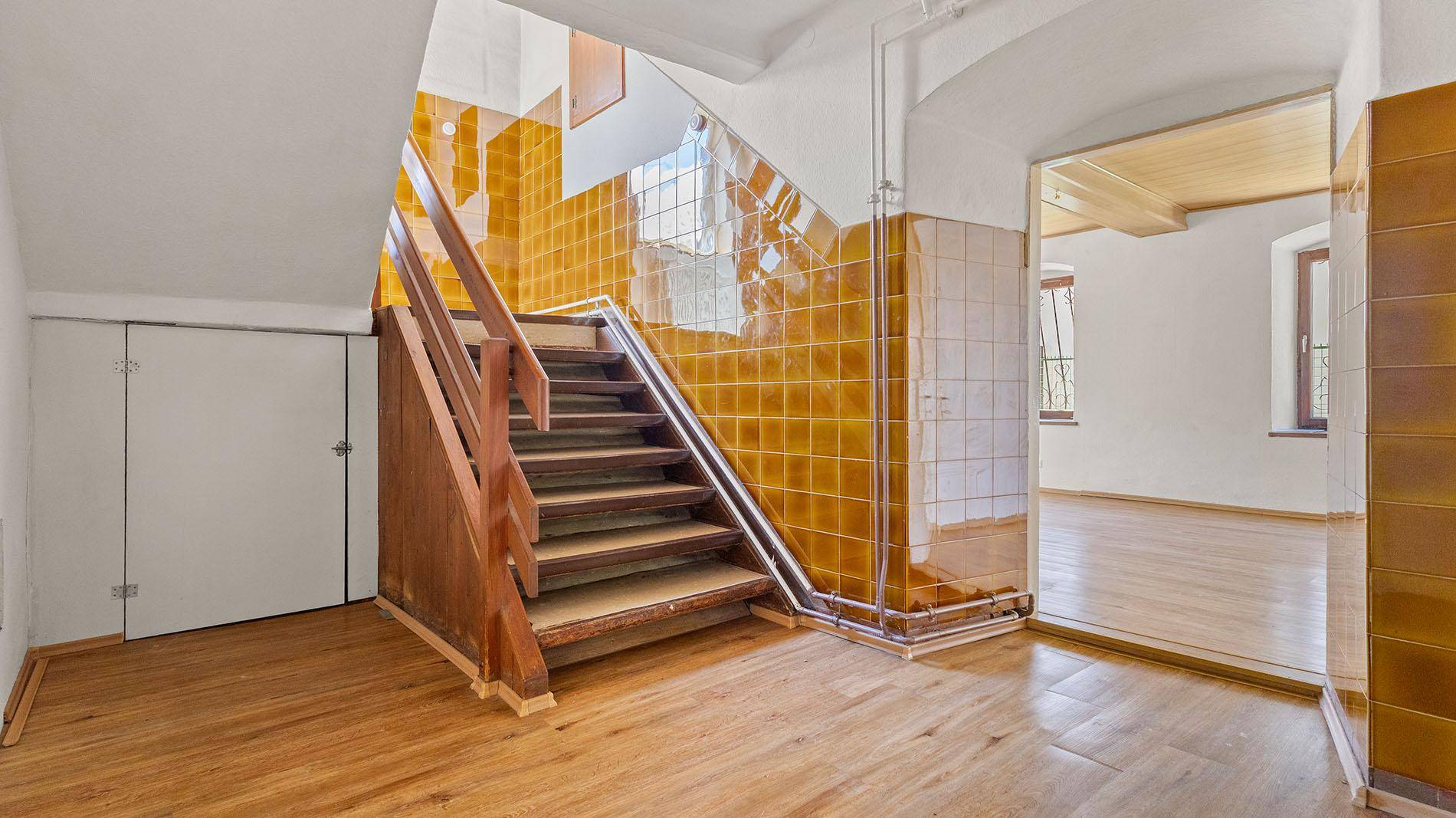 Treppenhaus mit Holztreppe und gelbbraunen Fliesen an den Wänden.