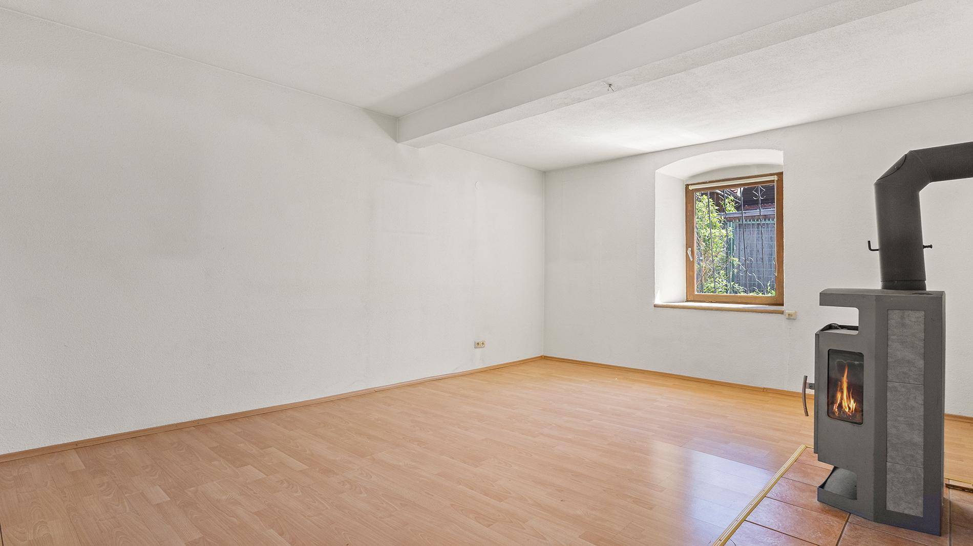 Geräumiges Wohnzimmer mit Holzboden und einem modernen Holzofen als Wärmequelle.
