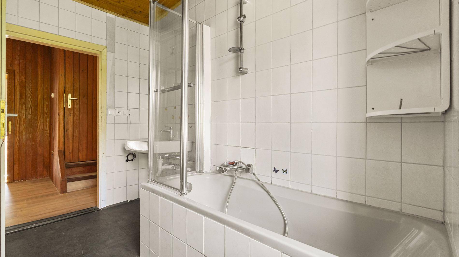 Badezimmer mit Badewanne, Duschabtrennung und weißen Wandfliesen.