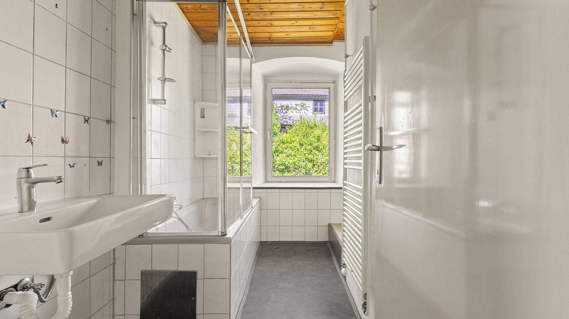 Helles Badezimmer mit Waschbecken, Badewanne und Fenster für Tageslicht.