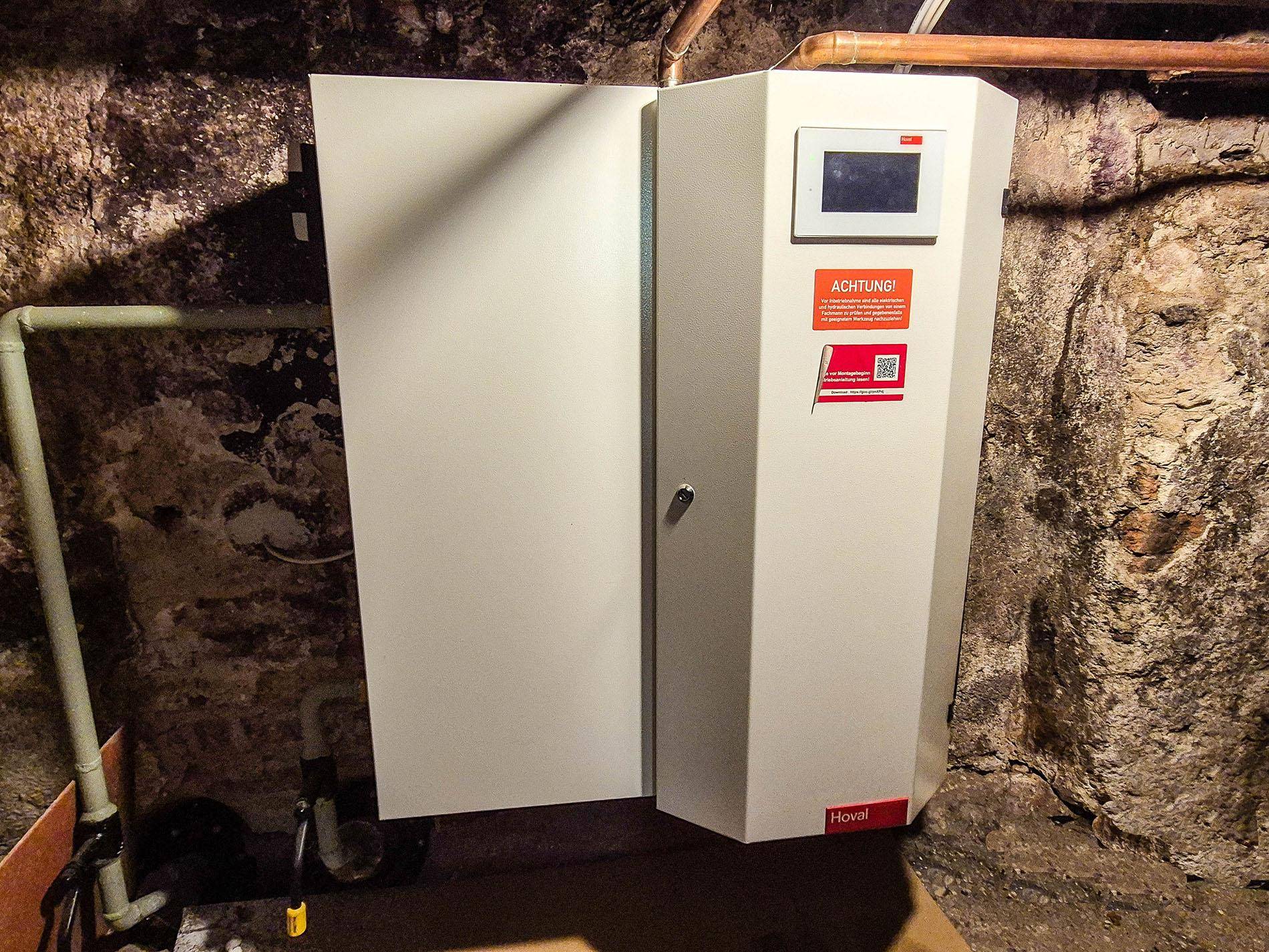 Moderne Heizungsanlage der Marke Hoval in einem Kellerraum mit Steinwänden.