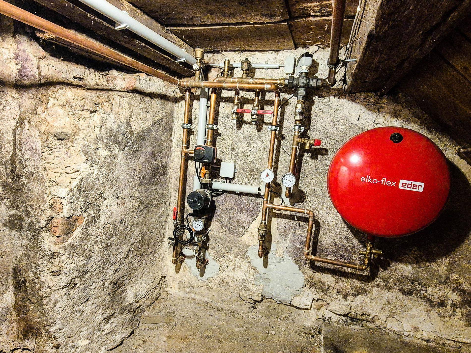Heizungsverteiler und Ausdehnungsgefäß in einem Kellerraum mit rustikalen Steinwänden.