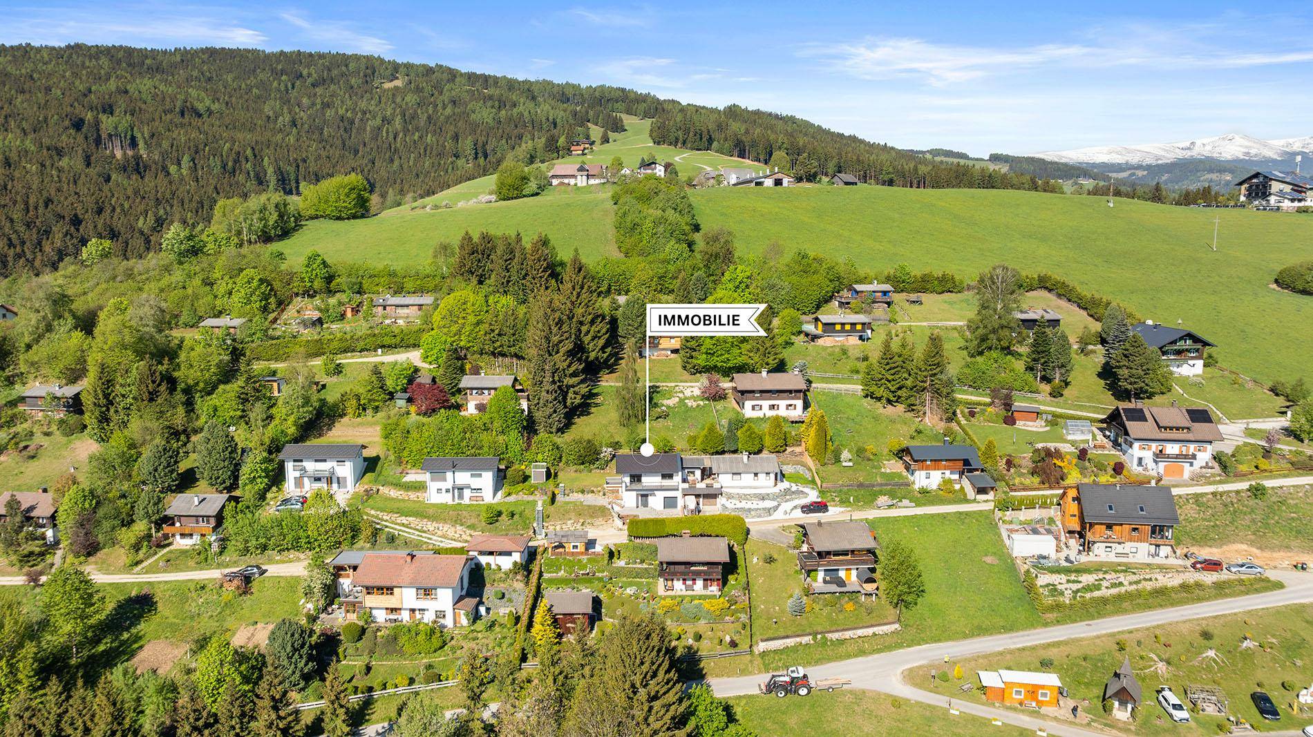 Weitläufige Luftaufnahme der Immobilie in einer grünen, hügeligen Umgebung mit Bergblick.