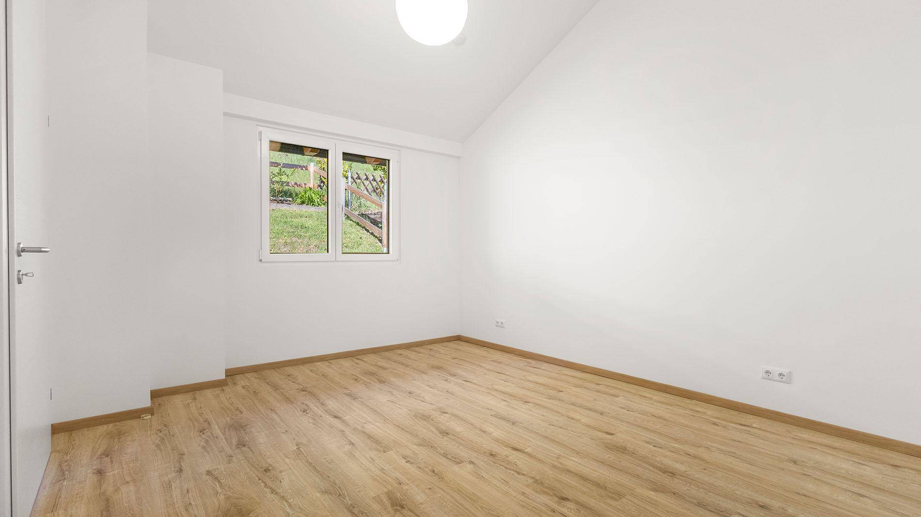 Helles Schlafzimmer mit Laminatboden, weiß gestrichenen Wänden und Fenster zum Garten.