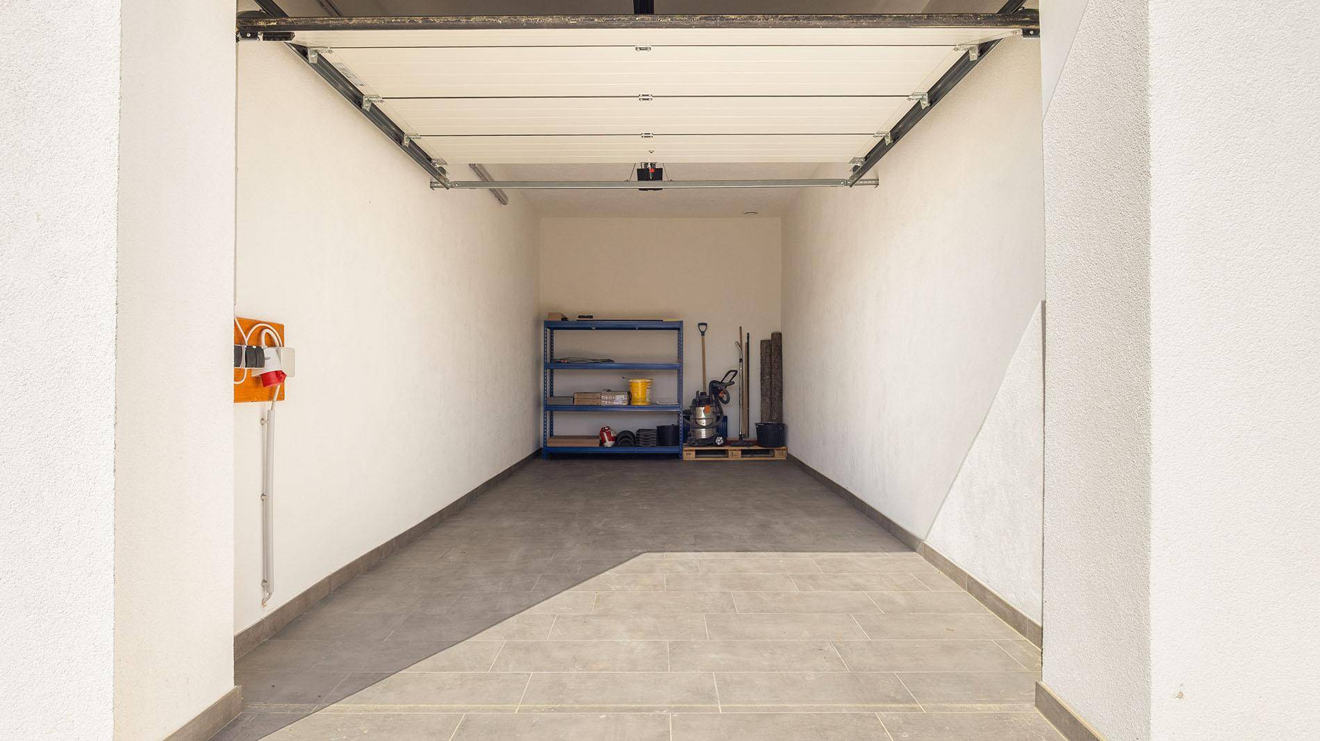 Geräumige Garage mit Fliesenboden und Stauraum für Fahrzeuge und Geräte.