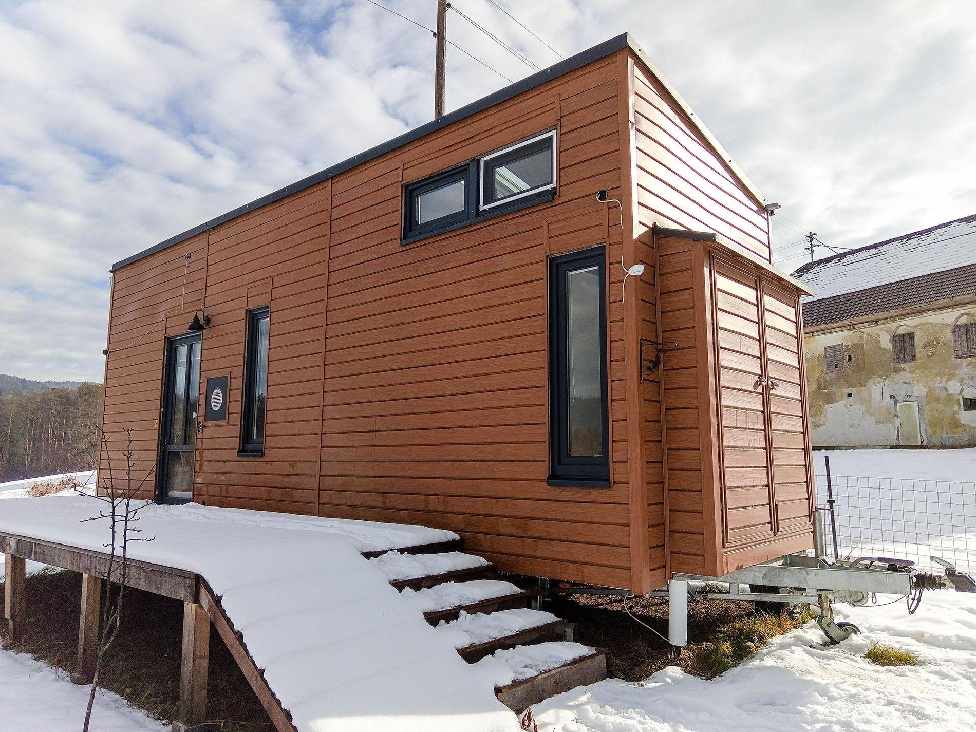Tiny House mit Holzfassade und kleiner Holzterrasse im winterlichen Landschaftsbild.