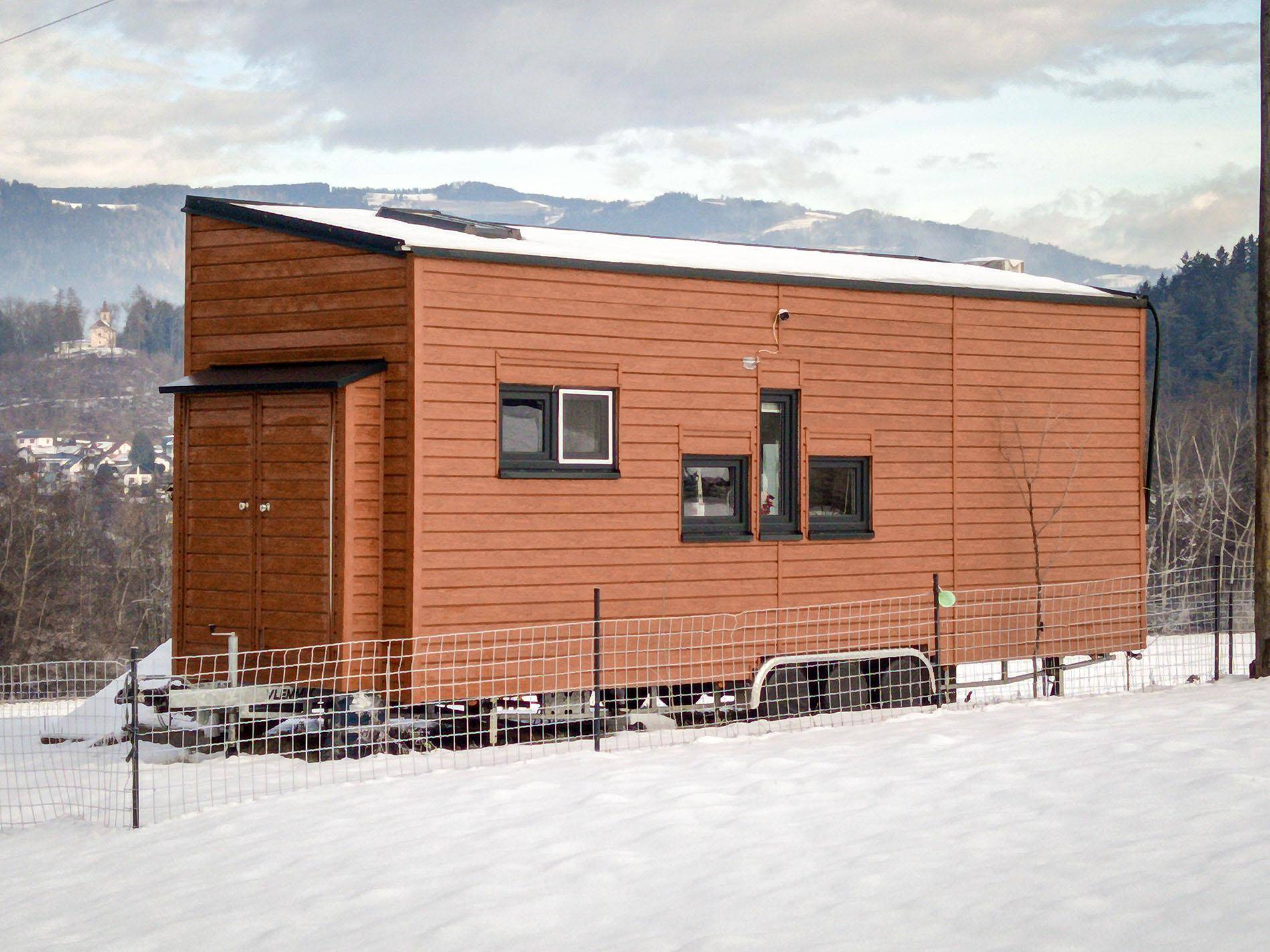Seitliche Ansicht des Tiny Houses mit Holzverkleidung, umgeben von verschneiter Landschaft.
