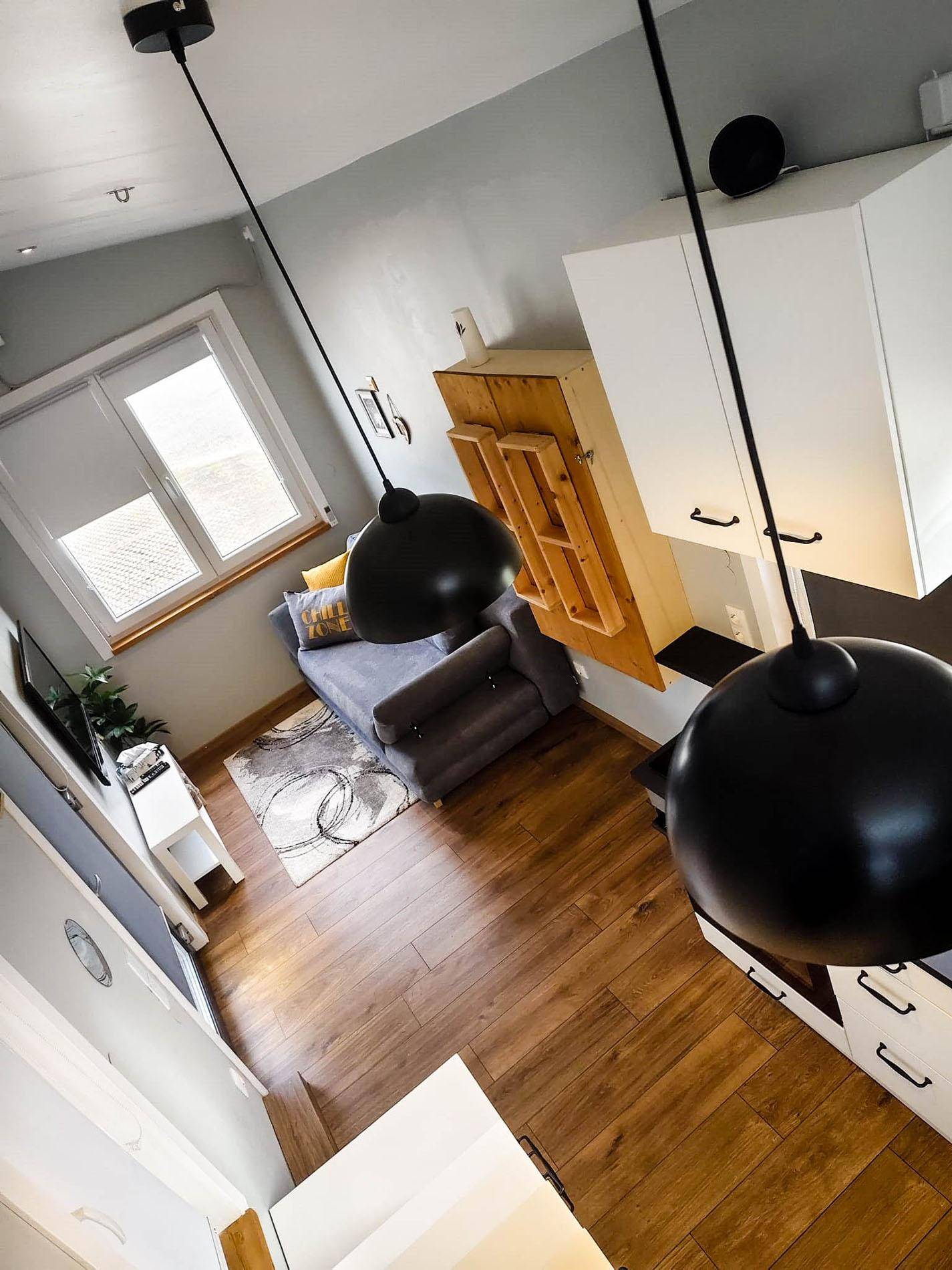 Gemütlicher Wohnbereich mit Sofa, Holzboden und modernen Pendelleuchten im Tiny House.