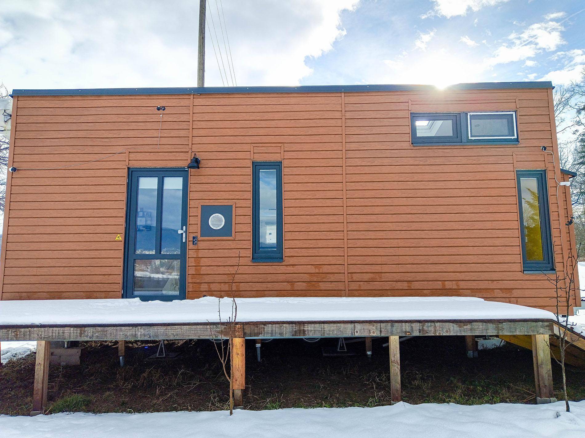 Längsseite des Tiny Houses mit Holzwänden und einer kleinen, schneebedeckten Holzplattform.