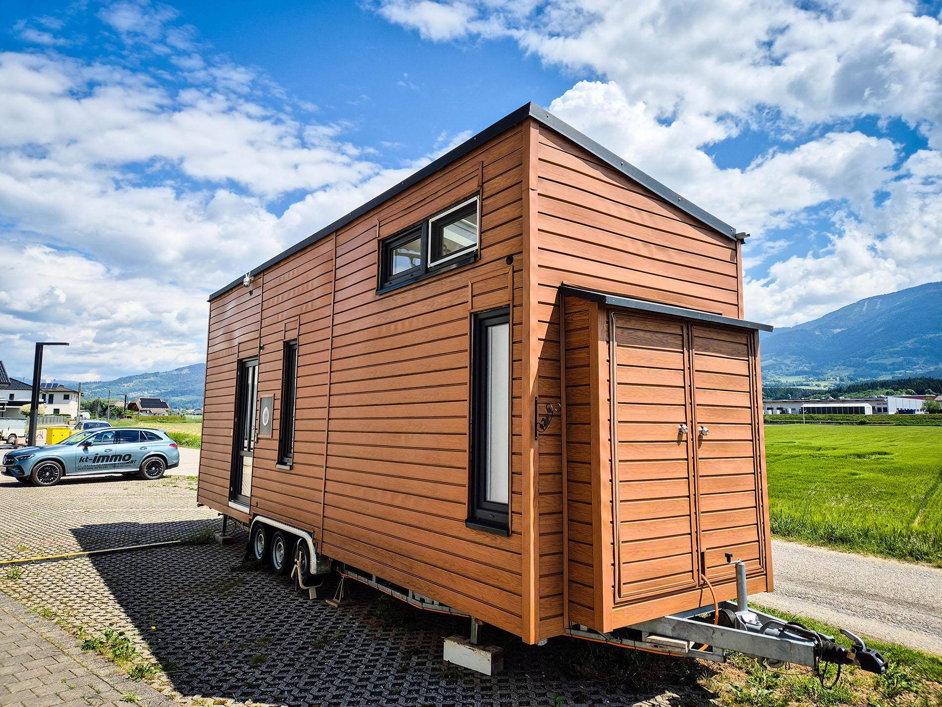 Vorderansicht des Tiny Houses mit Holzverkleidung und Anhängerkupplung in ländlicher Umgebung.
