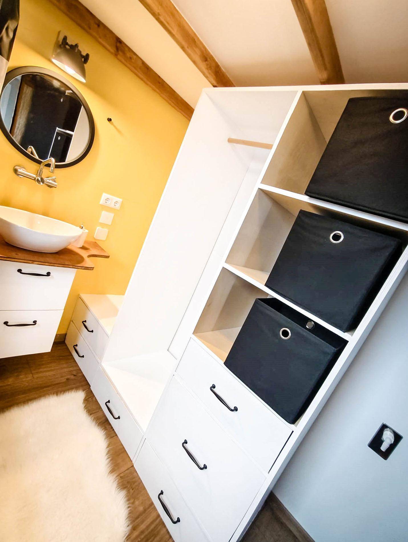 Badezimmer mit Waschbecken, Spiegel und integrierten Stauschränken unter der Dachschräge.