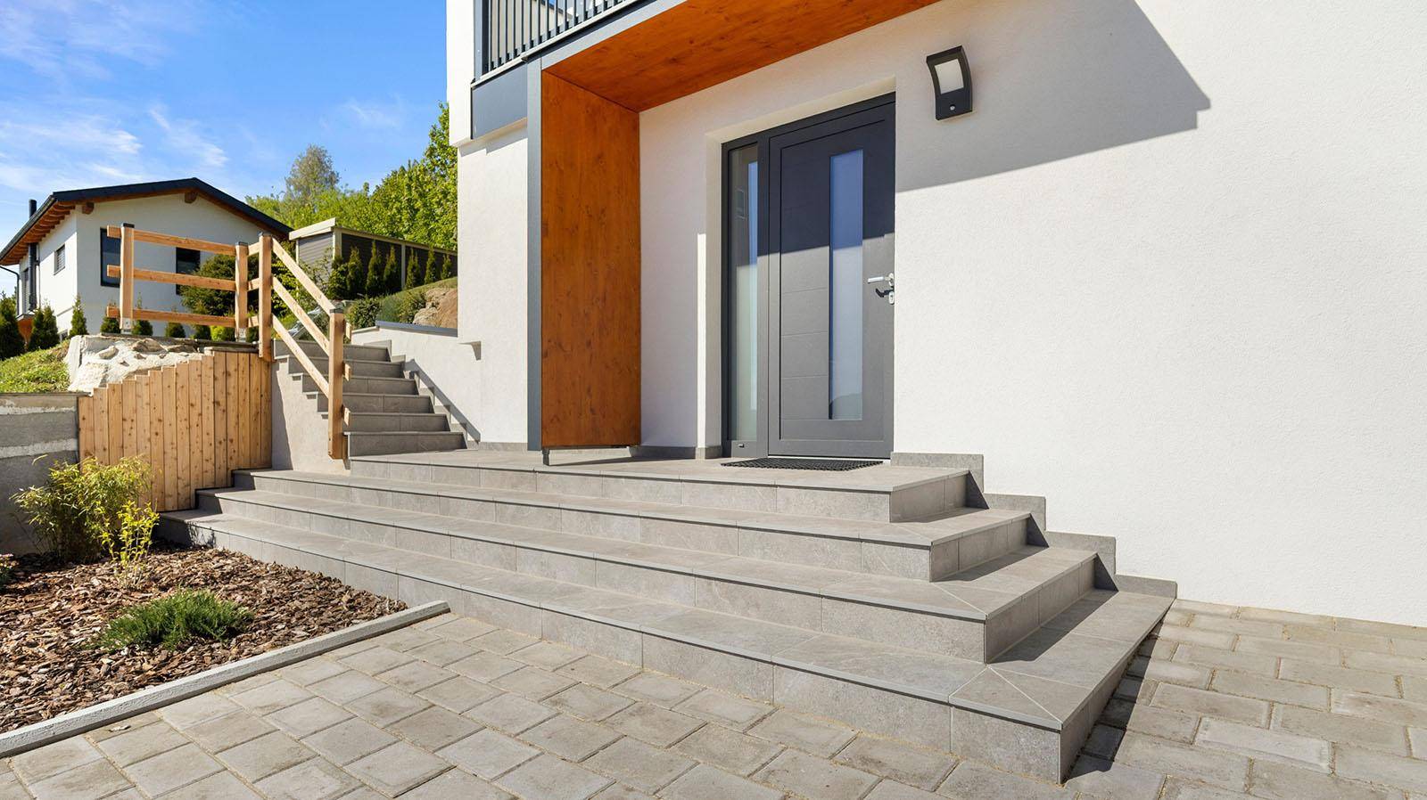 Moderner Hauseingang mit grauen Stufen, einer eleganten Haustür und gepflastertem Vorplatz.