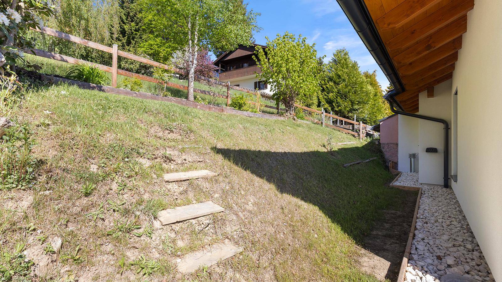 Grüner Hang mit Holzstufen und Zaun, der zum oberen Teil des Grundstücks führt, mit einem Haus im Hintergrund.