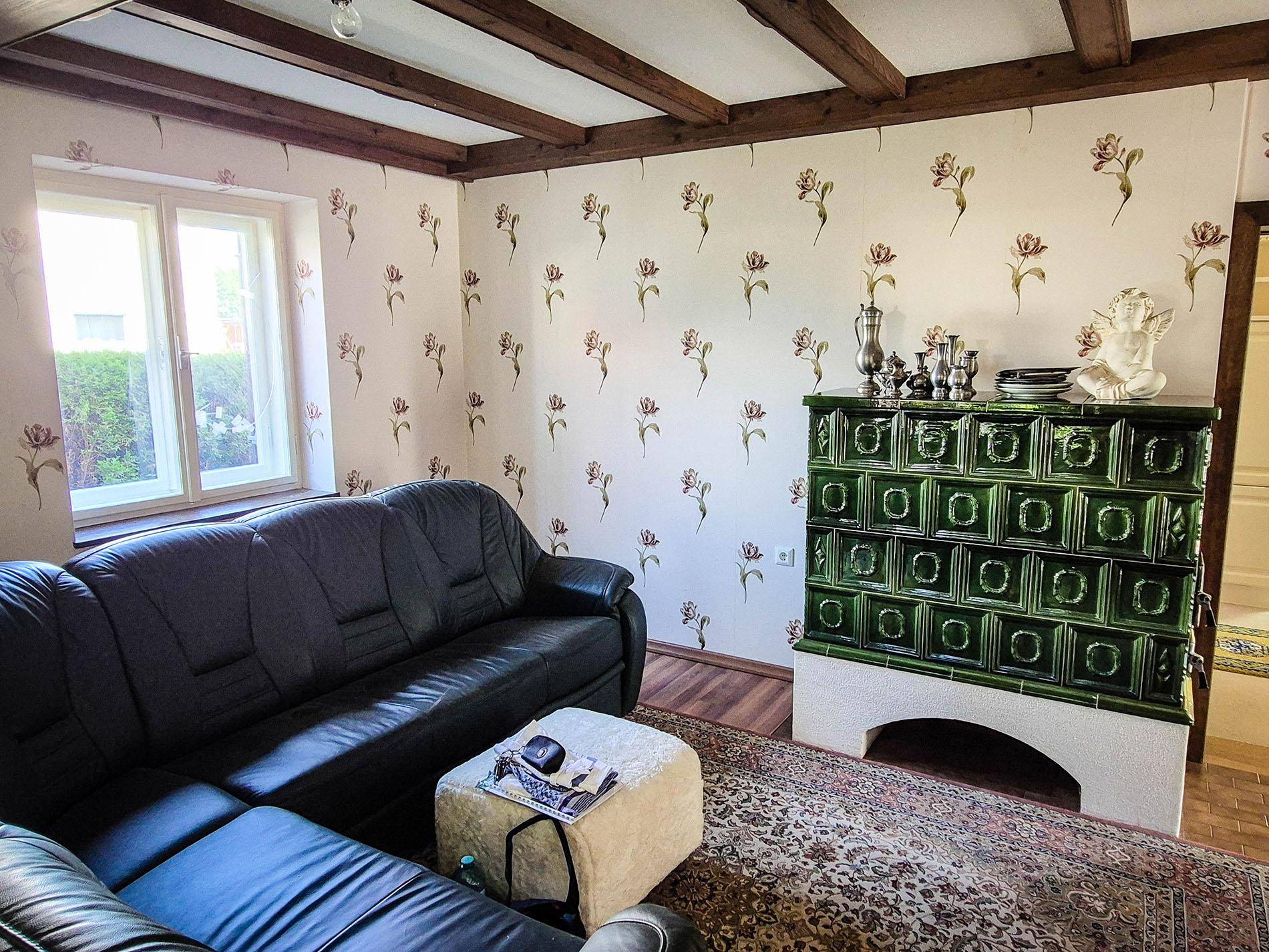 Gemütliches Wohnzimmer mit grünem Kachelofen, Sofa und floraler Tapete.